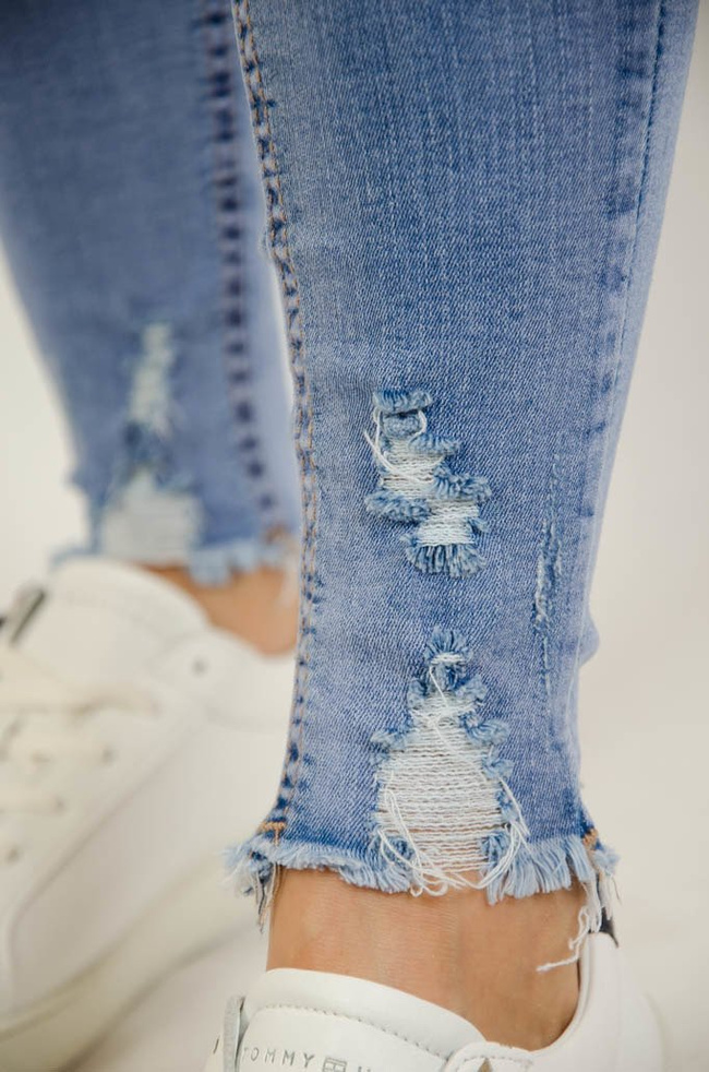 Jasne spodnie jeansowe z dziurami oraz szarpaniem przy nogawce