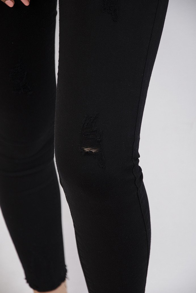 Czarne spodnie z przetarciami oraz szarpaniem przy nogawce