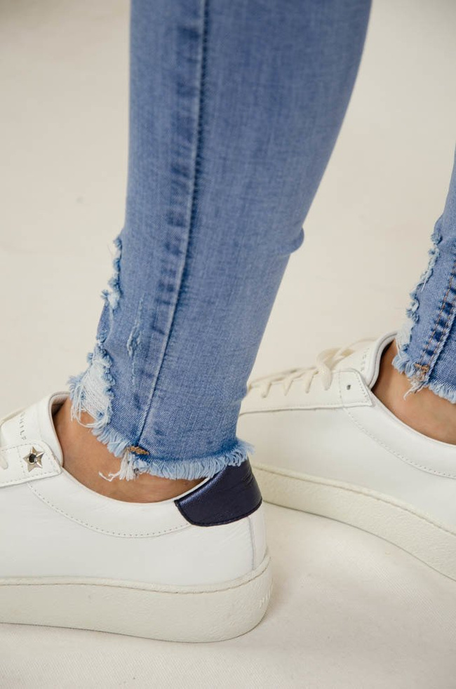 Jasne spodnie jeansowe z dziurami oraz szarpaniem przy nogawce