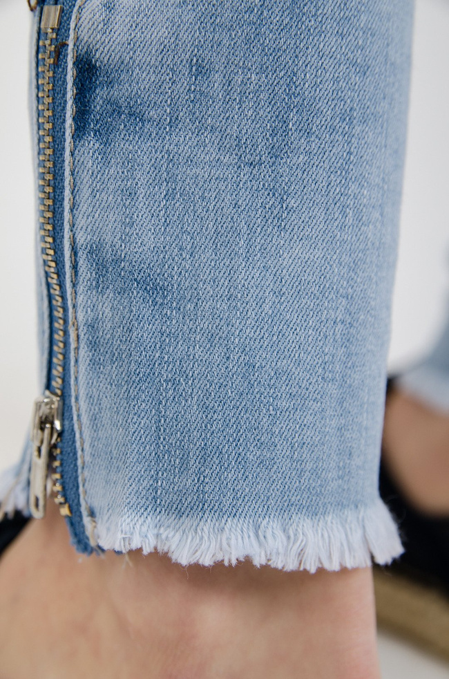 Jasne spodnie jeansowe z dziurami i zamkiem na nogawce