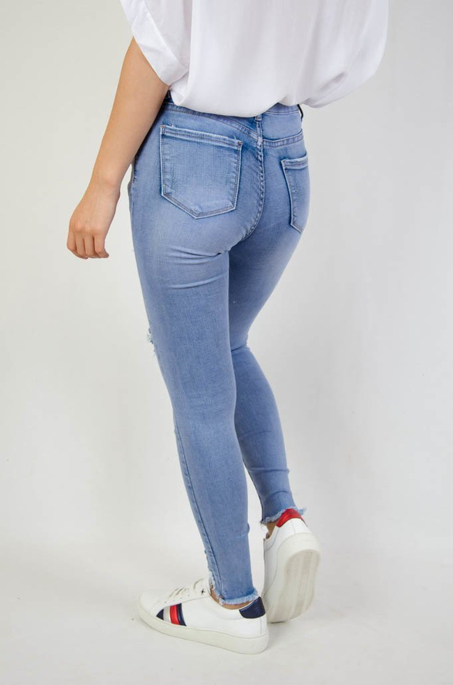 Jasne spodnie jeansowe z dziurami oraz szarpaniem przy nogawce