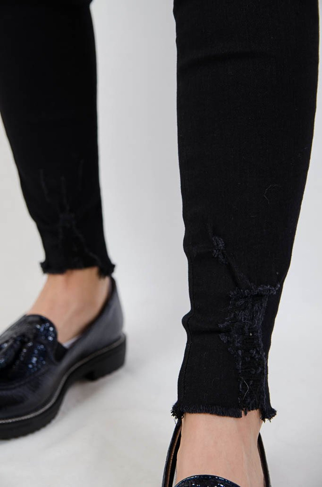 Czarne jeansowe spodnie z przetarciami oraz szarpaniem na dole nogawki