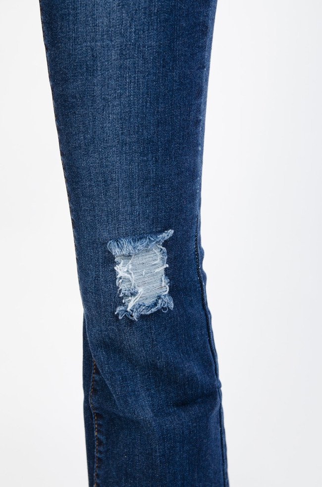 Ciemne spodnie jeansowe dzwony z poszarpaną nogawką