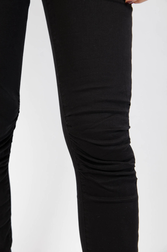 Czarne spodnie jeansowe z gumą w pasie oraz marszczeniem na kolanach