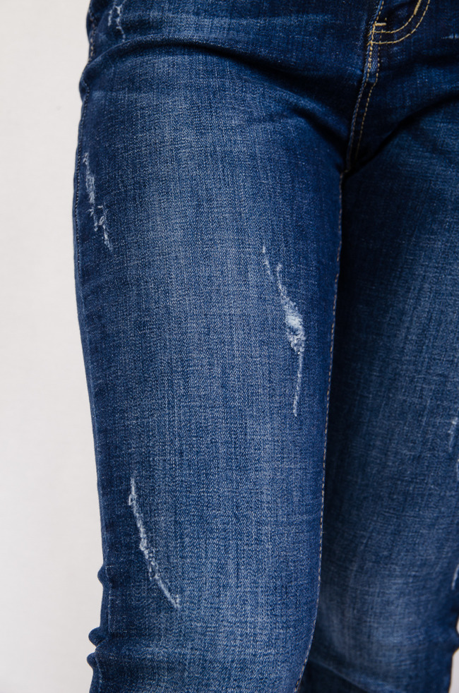 Spodnie jeansowe z licznymi przetarciami oraz naszywką na kieszeni